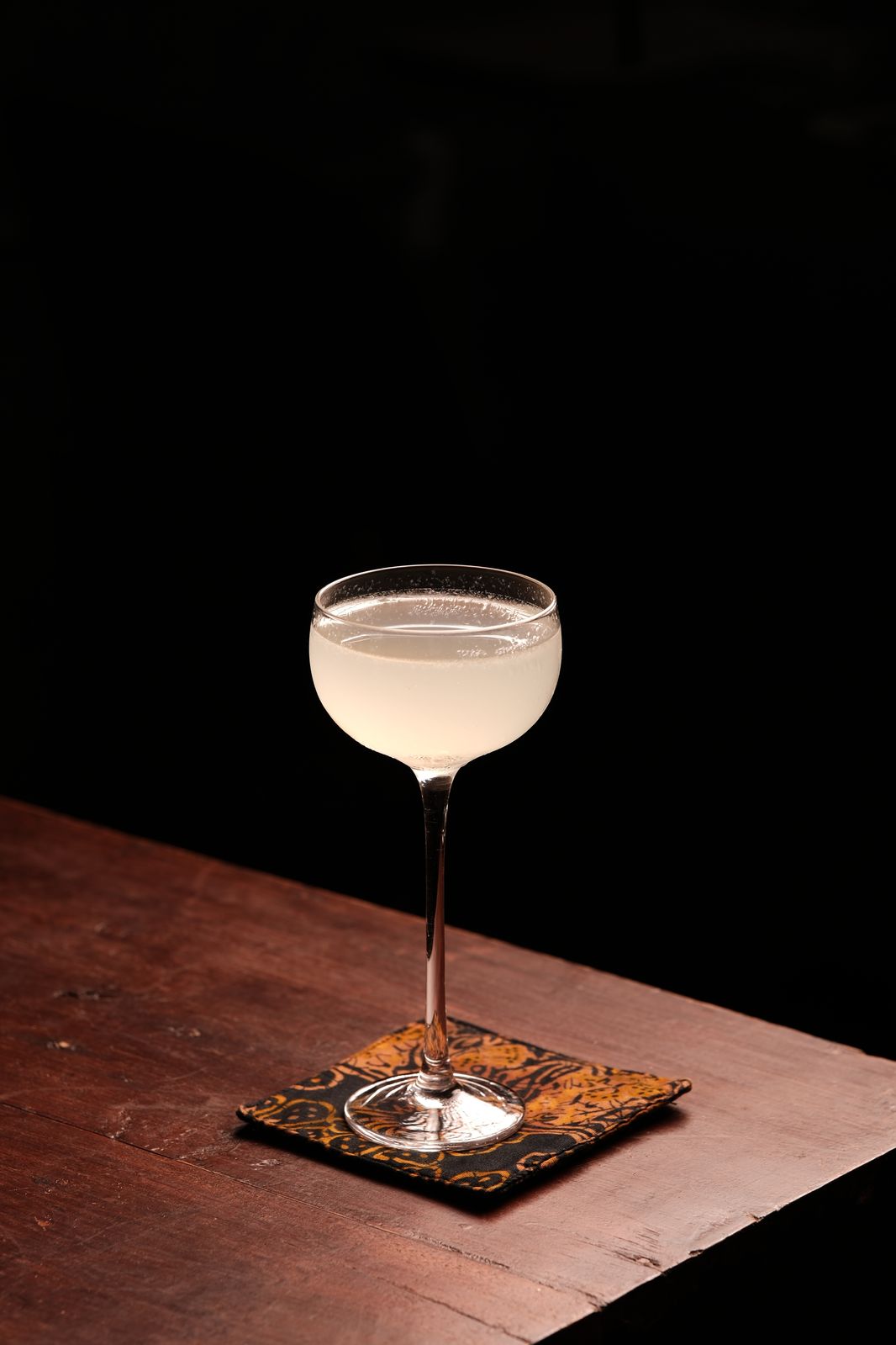A clear cocktail in a coupe glass on a batik coaster at Rembar