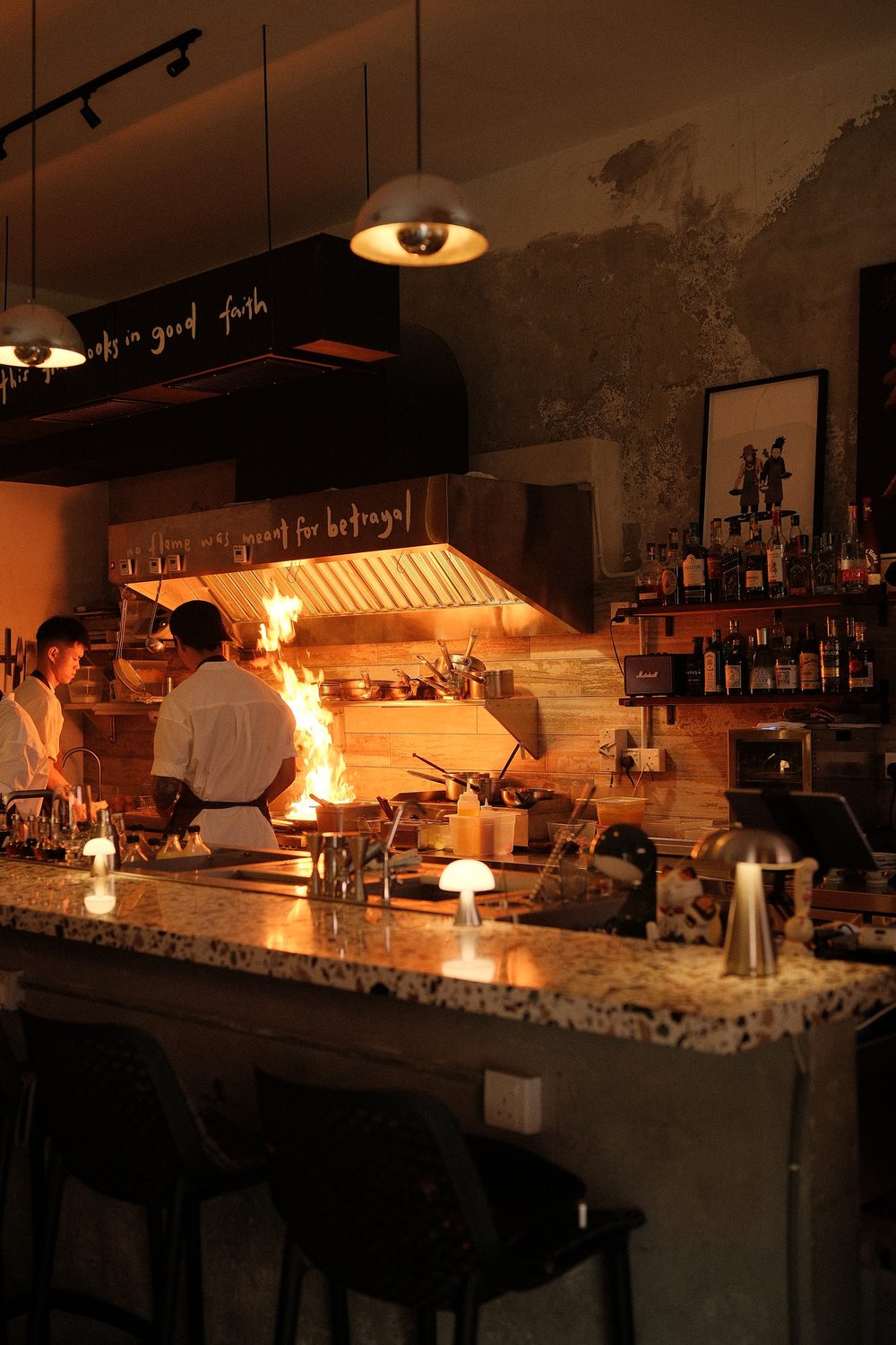 The open kitchen at Rembar, flames at the pass beneath the hood lettered 'no flame was meant for betrayal'